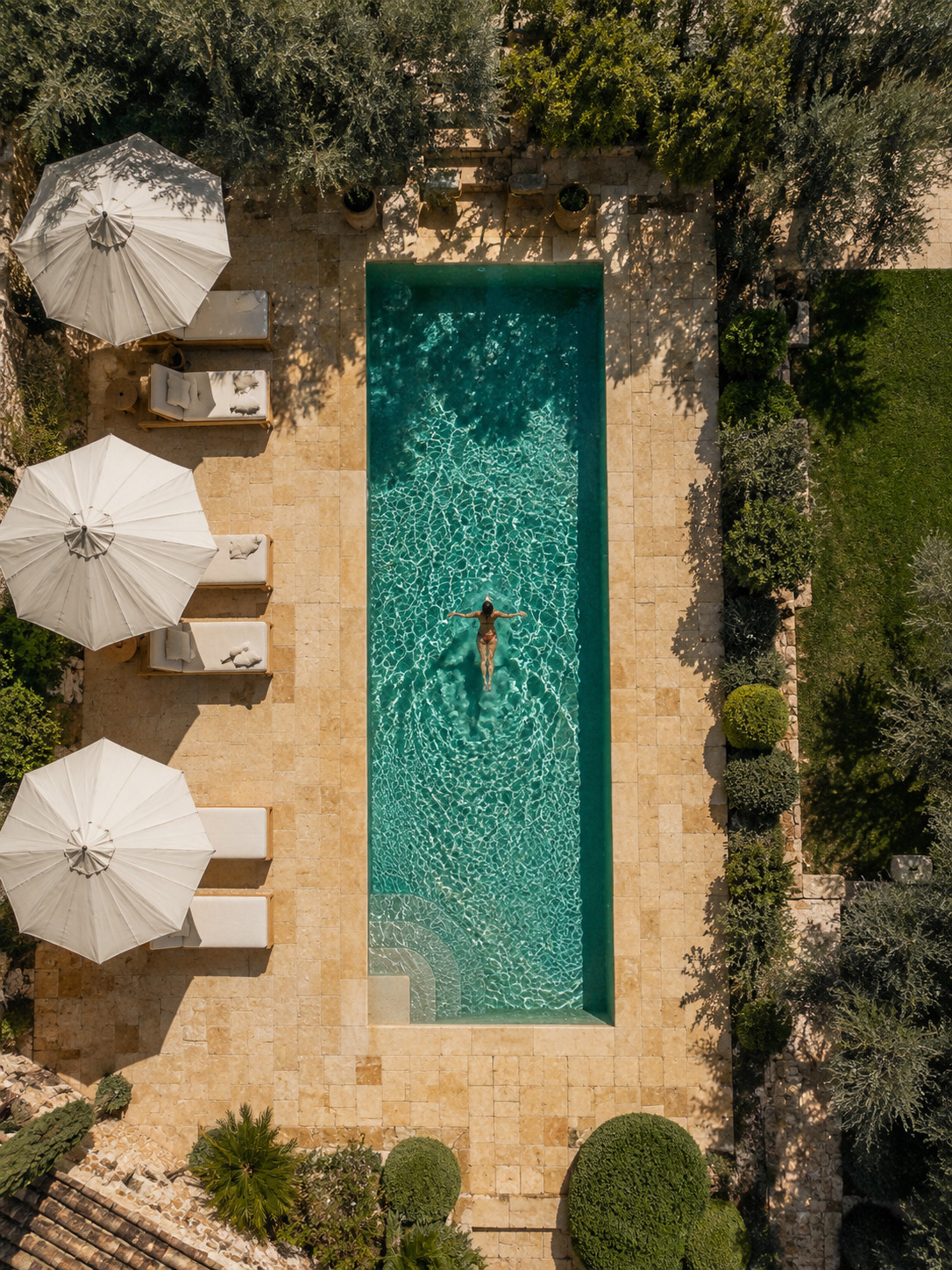Luftaufnahme einer Poolterrasse mit Travertin Terrassenplatten, Sonnenliegen und mediterraner Gestaltung